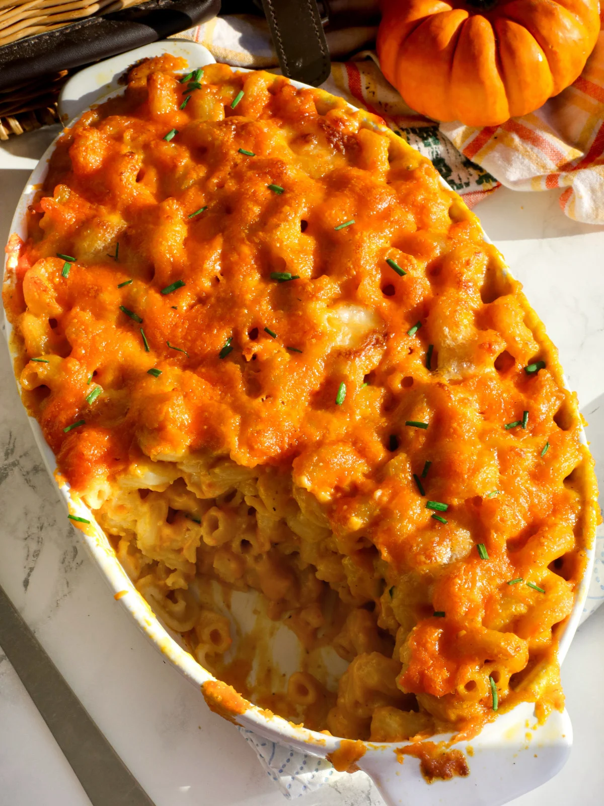Pumpkin macaroni and cheese in an oval white oven dish on a table with chives Pumpkin Recipes