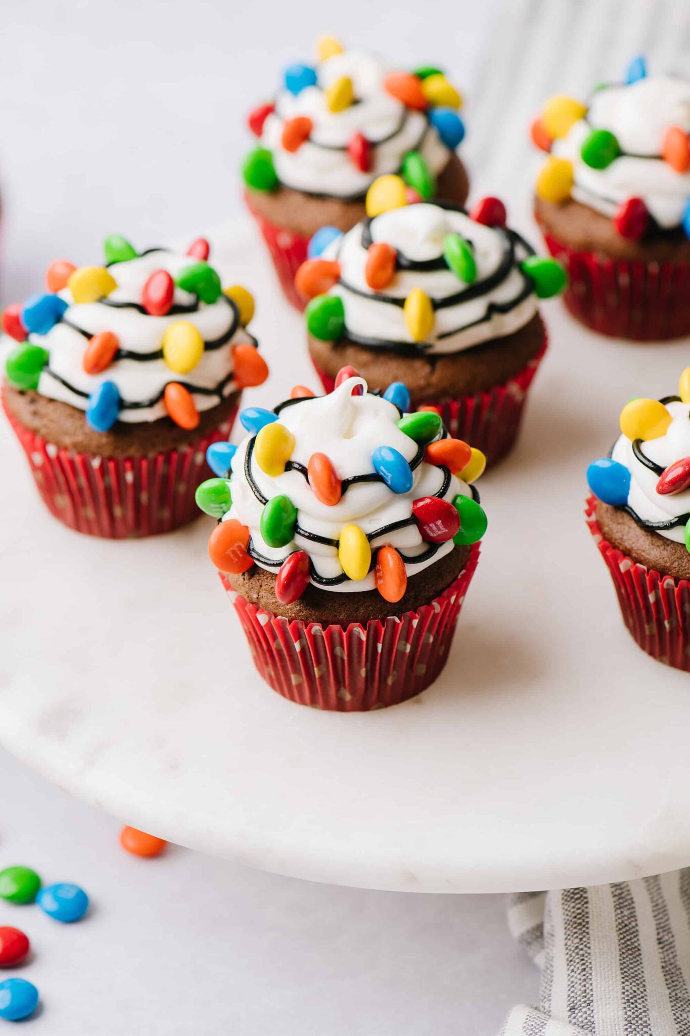 24 Easy & Creative Christmas Cupcakes to Try Right Now 54 24 Easy & Creative Christmas Cupcakes to Try Right Now Christmas light cupcakes with white frosting, black icing strings, and colorful candy lights