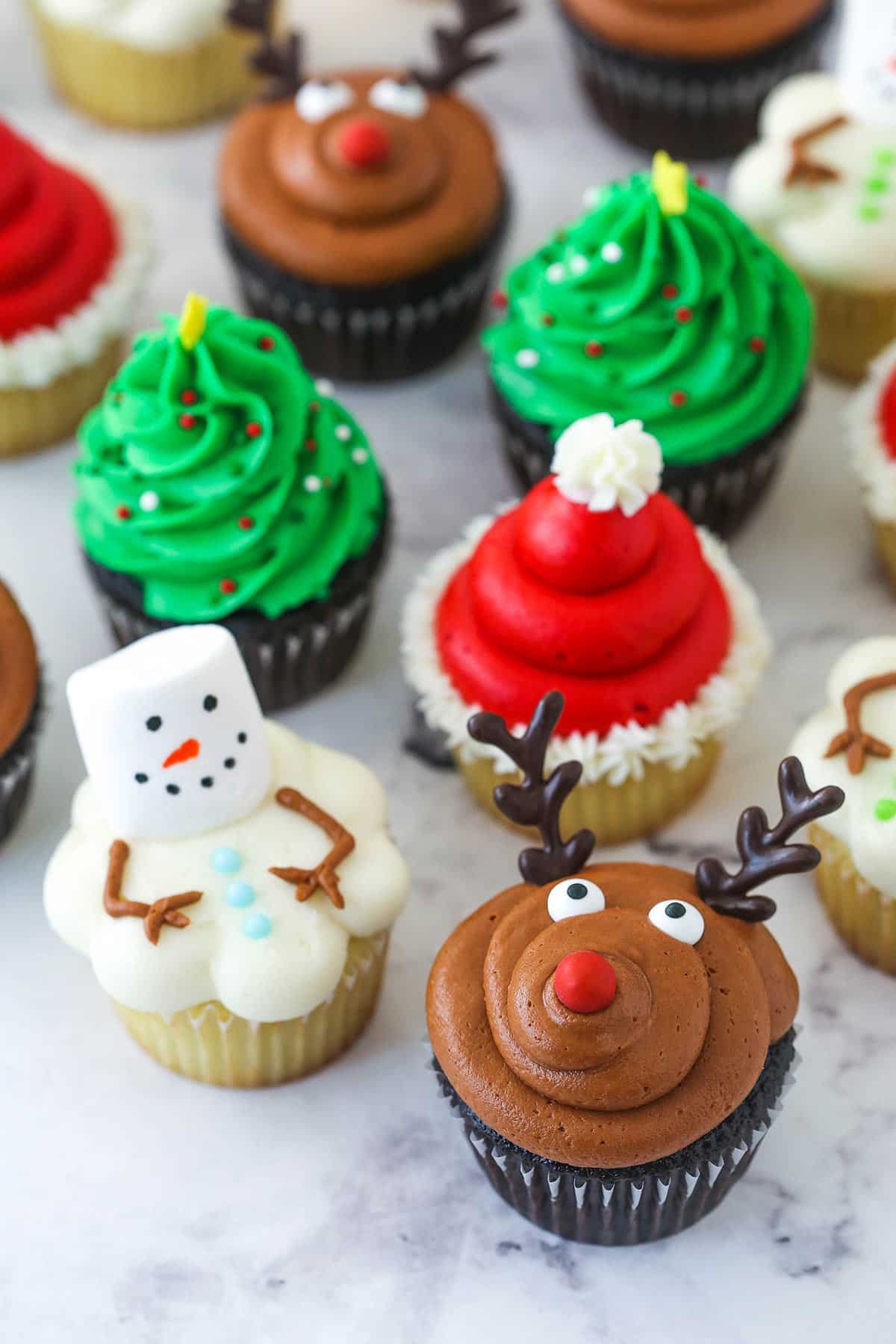 24 Easy & Creative Christmas Cupcakes to Try Right Now 56 24 Easy & Creative Christmas Cupcakes to Try Right Now Assorted Christmas cupcakes decorated as reindeer, snowmen, Santa hats, and Christmas trees