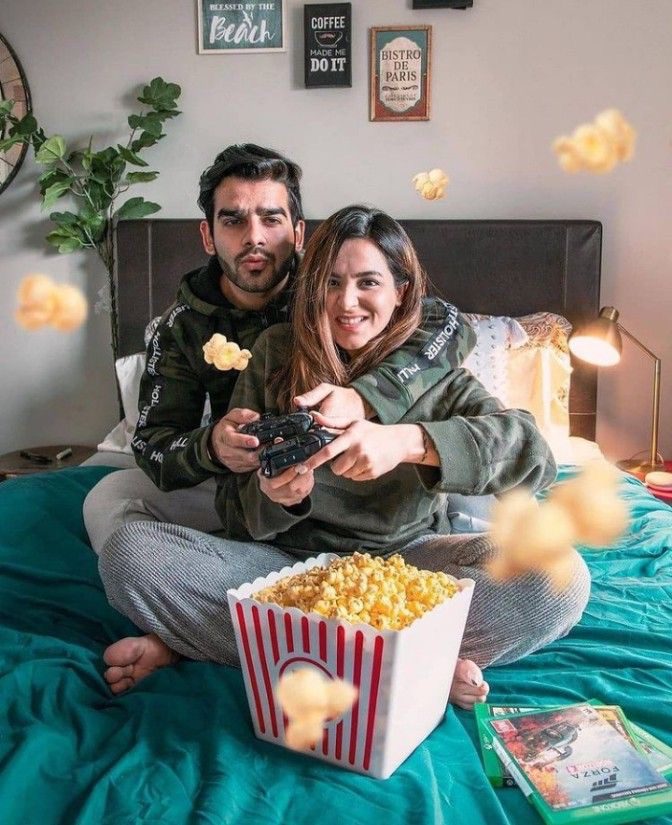 Couple playing video games together with controllers and a large tub of popcorn