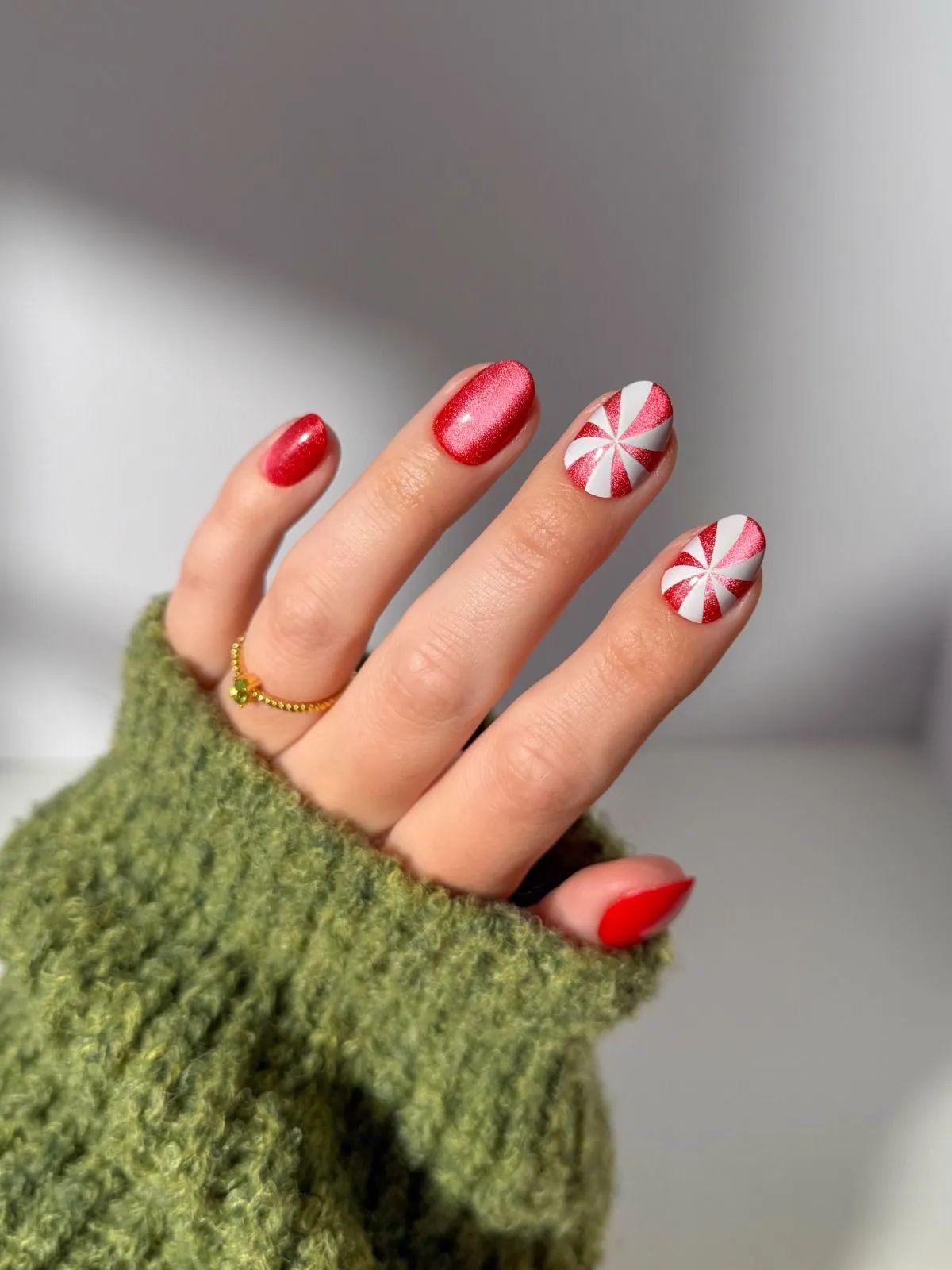 Short Christmas nails with red shimmer polish and white peppermint candy swirl accents