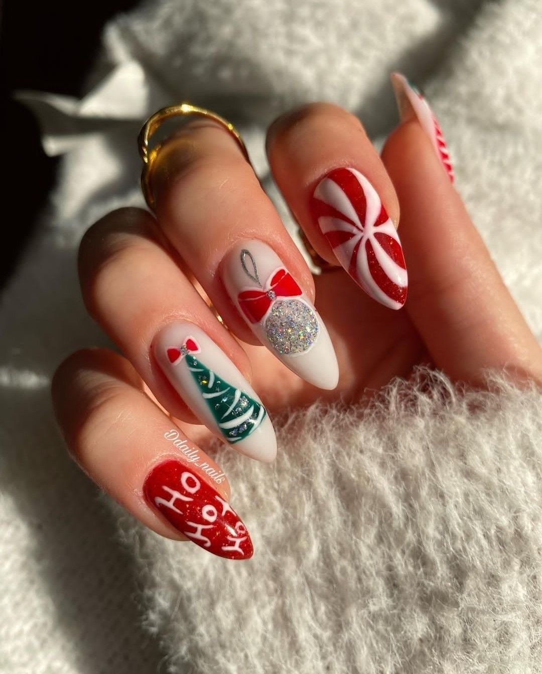 Christmas almond nails featuring a green tree, glitter ornament, red peppermint swirl, and festive lettering