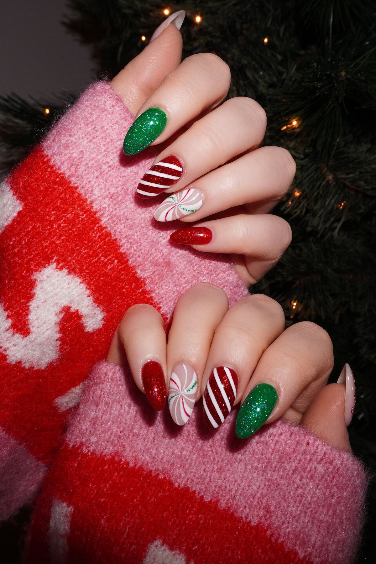 Festive almond nails with green glitter, red candy cane stripes, and pink peppermint swirl designs