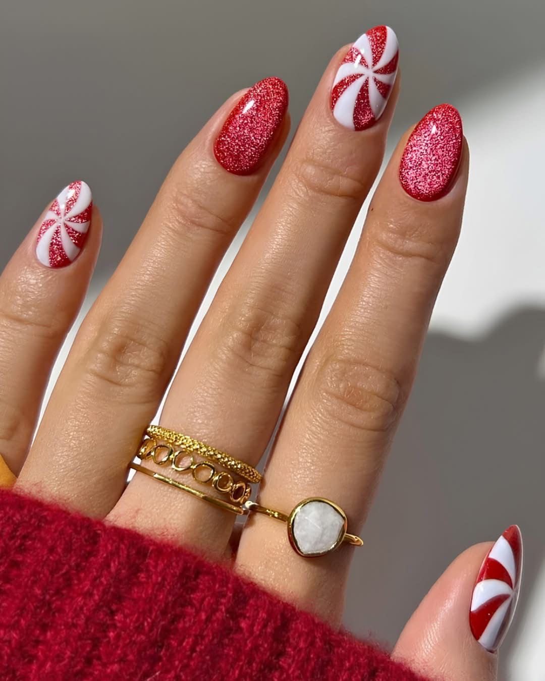 Short almond nails with red glitter polish and white peppermint swirl accent designs