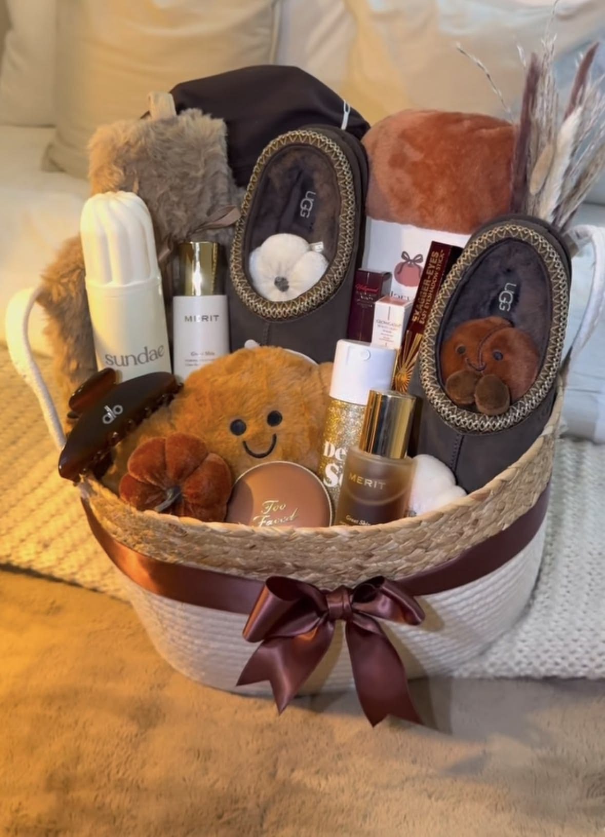 30 Thoughtful Christmas Gift Basket Ideas for Her 72 30 Thoughtful Christmas Gift Basket Ideas for Her Neutral winter gift basket with dark slippers, a rolled throw, beauty products and a small plush toy