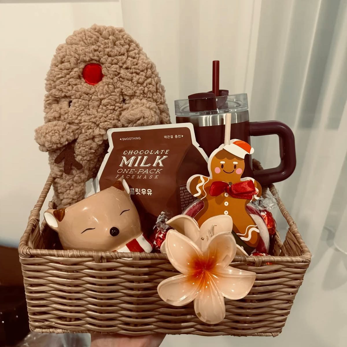 30 Thoughtful Christmas Gift Basket Ideas for Her 82 30 Thoughtful Christmas Gift Basket Ideas for Her Wicker Christmas basket with a gingerbread plush, brown handled tumbler, chocolate face mask and festive accessories