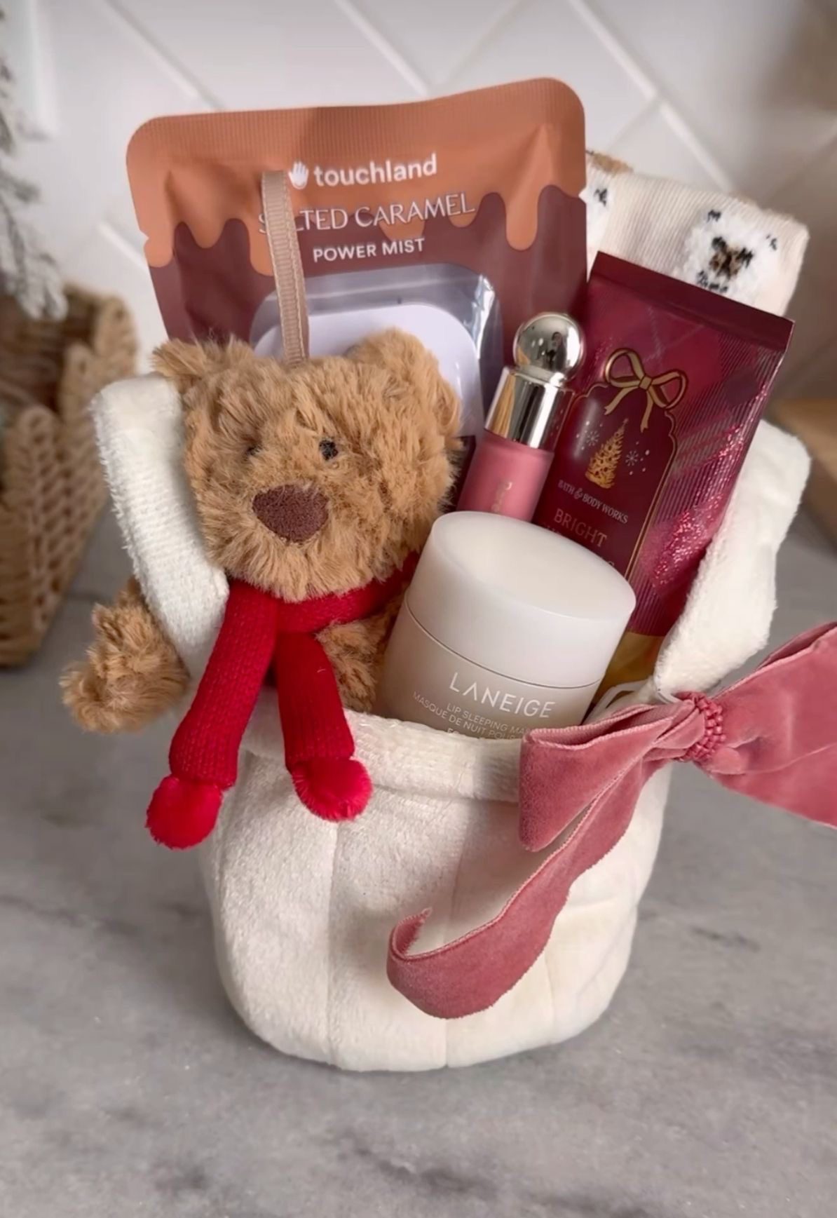 30 Thoughtful Christmas Gift Basket Ideas for Her 83 30 Thoughtful Christmas Gift Basket Ideas for Her Small cream gift basket with a teddy bear in a red scarf, hand sanitiser, beauty products and a pink bow