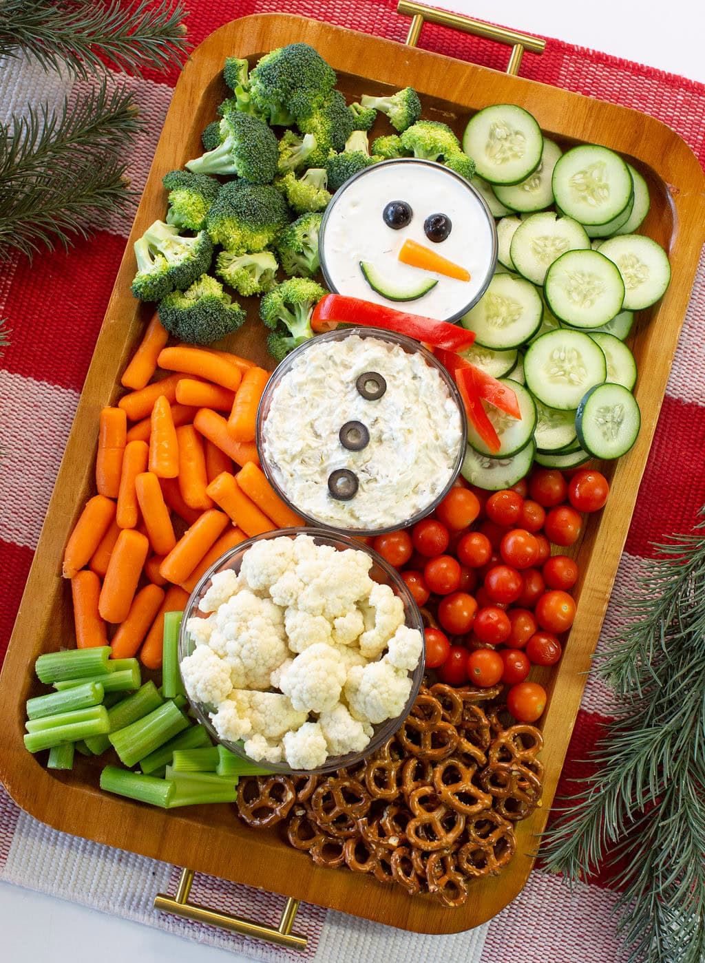 Christmas snowman veggie tray with three round bowls, broccoli, carrots, cucumber, cauliflower and pretzels