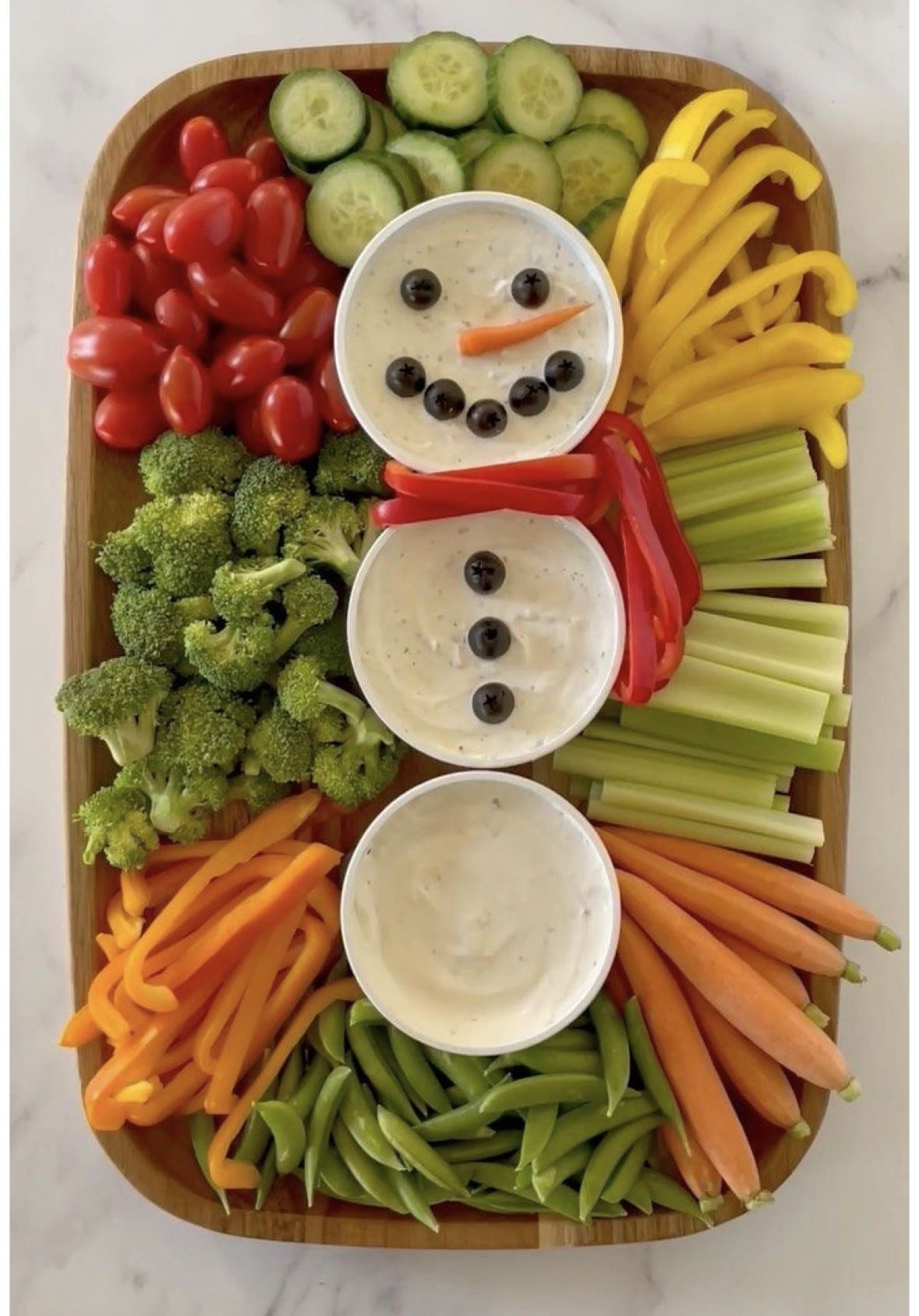 Snowman Christmas vegetable platter with three dip bowls surrounded by tomatoes, cucumber, peppers, celery, broccoli, carrots and snap peas