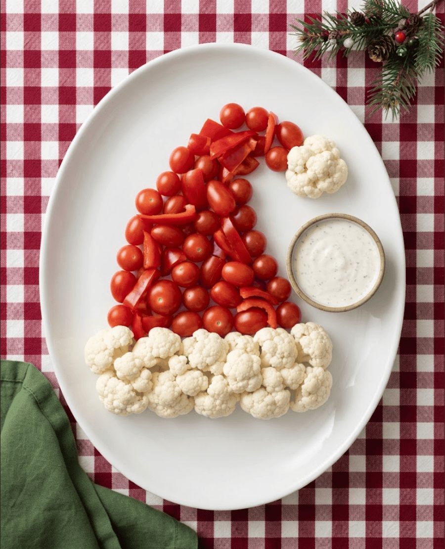 Santa hat-shaped vegetable platter made with red cherry tomatoes, red peppers, cauliflower trim and a bowl of creamy dip