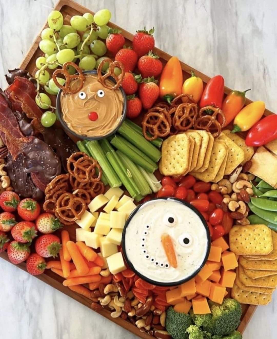 Festive grazing board with reindeer dip, snowman dip, strawberries, grapes, peppers, cheese, crackers, celery and pretzels
