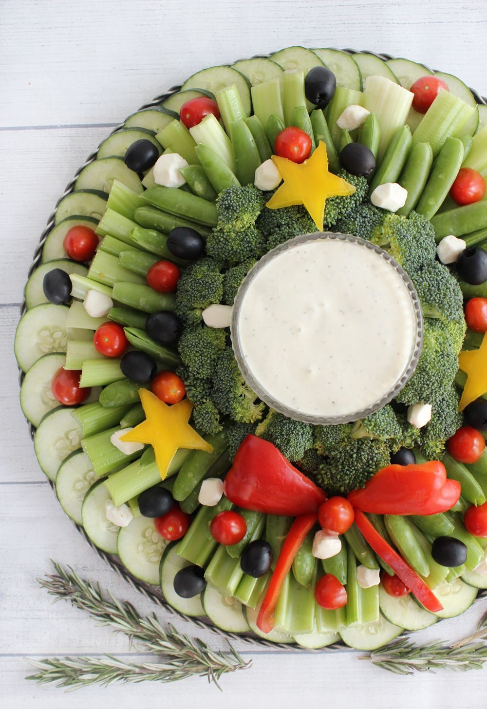 Christmas vegetable wreath with cucumber slices, celery, snap peas, broccoli, black olives, tomatoes, yellow pepper stars and a red pepper bow