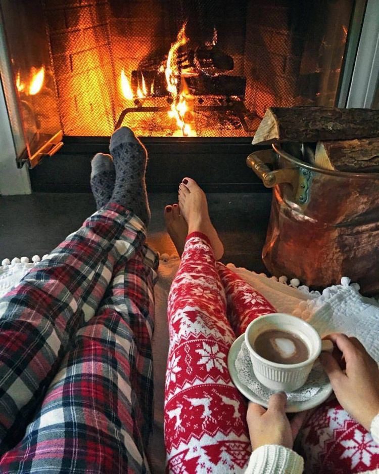 Couple in Christmas pyjamas enjoying hot drinks beside a glowing fireplace