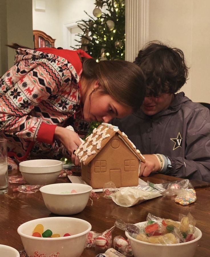 Couple decorating a gingerbread house together with icing and sweets