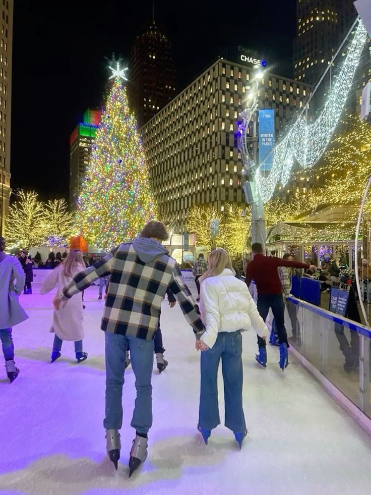 Couple holding hands while ice skating beside a brightly lit Christmas tree