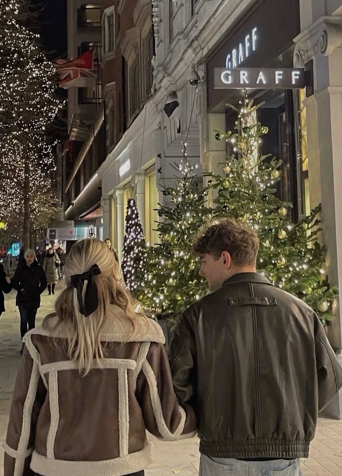 Couple walking past elegant shops decorated with Christmas trees and lights