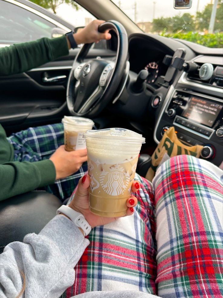 Couple holding takeaway coffees in a car while wearing cosy festive clothes
