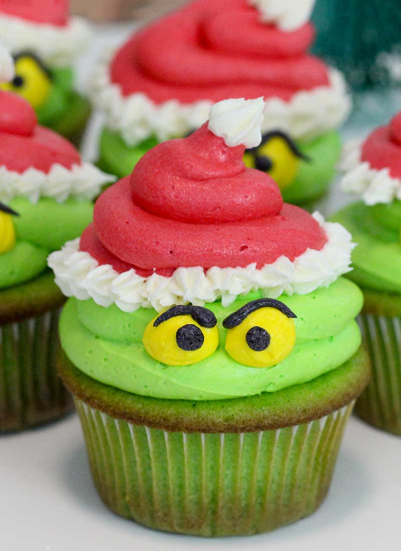 24 Easy & Creative Christmas Cupcakes to Try Right Now 58 24 Easy & Creative Christmas Cupcakes to Try Right Now Grinch cupcakes with green frosting, yellow eyes, black eyebrows, and red Santa hats
